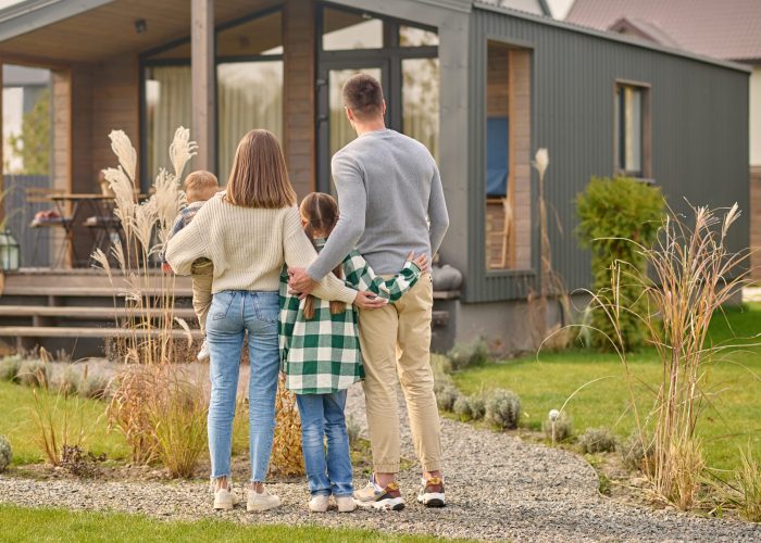 Back view of family hugging and admiring their home Happy family. View from back of man woman with child and girl standing together hugging and admiring their cozy home on fine autumn day